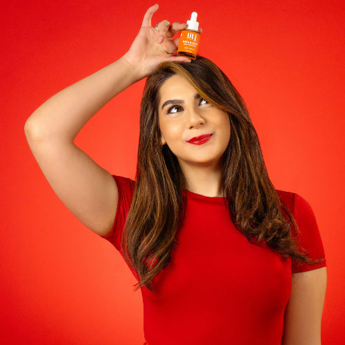 Woman holding a bottle of hair product above her head against a red background
