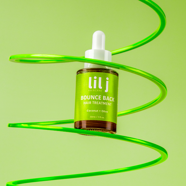 A hair oil treatment bottle with a green and white label, branded 'lil j', on a green background with a spiral pattern.