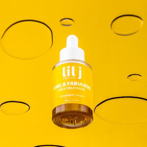 A yellow bottle of 'Fine & Fabulous Hair Treatment' by lil j with a white dropper cap, displayed on a yellow background with circular cut-outs.